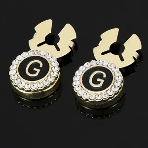 Detail of round gold cufflinks with black disk, letter G, and sparkling white rhinestones