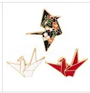 Detailed view of three origami crane enamel pins in black floral, white, and red with gold edges