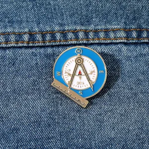 Detailed close-up of a blue enamel alloy compass and ruler brooch on denim fabric