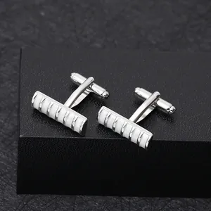 Detail of silver business cufflinks with white enamel inlay on a black textured background