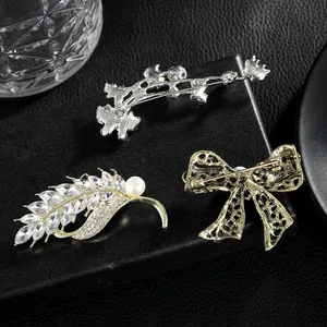 Detailed front and back view of crystal wheat ear and bow brooches on dark leather