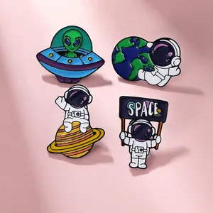 Detailed close-up of four space-themed enamel pins featuring astronauts and aliens on a pink background