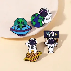 Close-up of enamel space pins showing an astronaut on Saturn and a green UFO