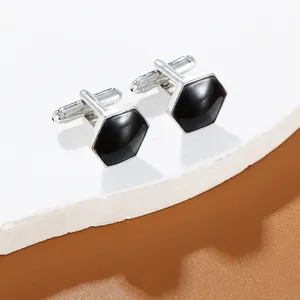 Detail of silver hexagonal cufflinks with black inlay on a white stone pedestal