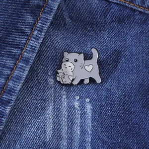 Broche mignonne en émail d'un chat gris portant un chaton sur du tissu denim