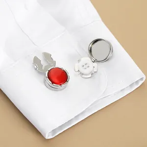 Detalle de cubrebotones plateados con gemas rojas en el puño de una camisa blanca