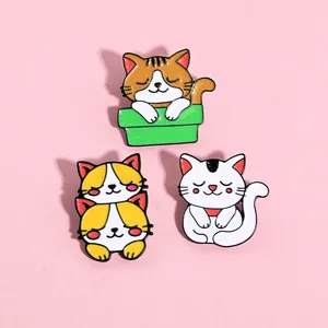 Dettaglio di tre simpatiche spille in smalto con gatti su uno sfondo rosa