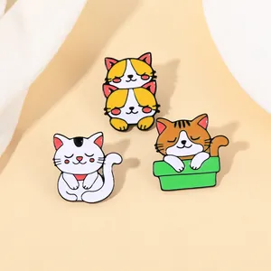 Dettaglio di tre spille in smalto con gatti carini che mostrano gattini che dormono su beige