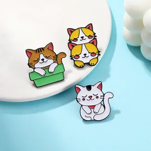 Dettaglio di tre simpatiche spille in smalto a forma di gatto su piatto di ceramica