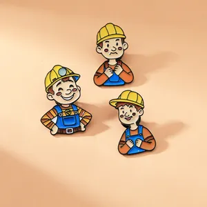 Detailed view of three cartoon worker enamel pins with yellow helmets on a pink surface