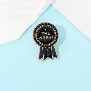 Close-up of medal-shaped black enamel brooch with THE WORST and YAY gold text