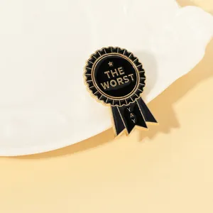 Close-up of a gold and black medal-shaped enamel pin featuring THE WORST and YAY text