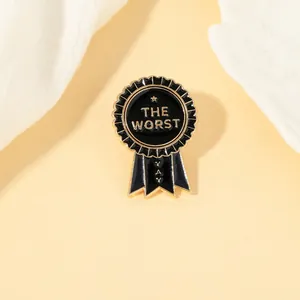 Close-up of medal-shaped enamel brooch featuring THE WORST and YAY text in black and gold