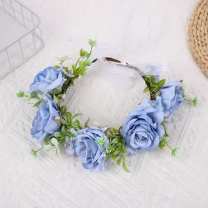 Detail of blue fabric rose crown featuring green leaves and adjustable white silk ribbons