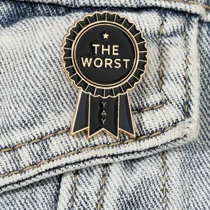 Black and gold enamel medal brooch with THE WORST text on denim fabric background