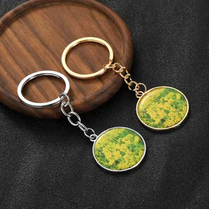 Detail of silver and gold keychains featuring yellow rapeseed flower glass cabochon pendants
