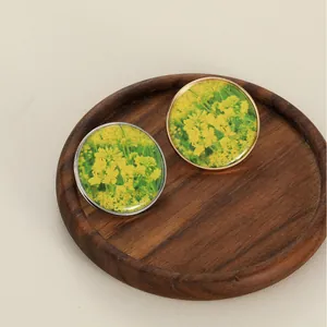 Detail of rapeseed flower jewelry charms with gold and silver metal frames on wood