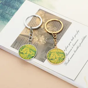 Detailed view of round rapeseed flower resin keychains in gold and silver metal frames