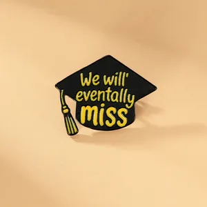 Close-up of black graduation cap enamel pin with yellow tassel and We will eventually miss text