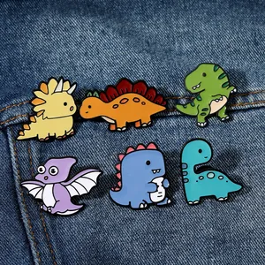 Set of six colorful enamel dinosaur pins displayed on dark blue denim fabric texture