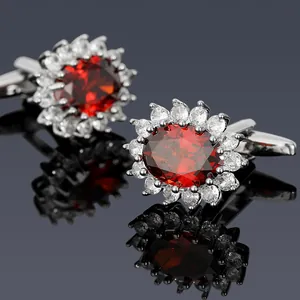 Macro view of silver cufflinks with oval red zircon and clear stone halo on black surface
