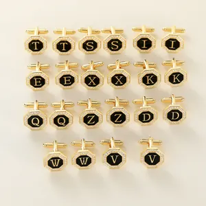 Detalle de gemelos dorados octogonales con esmalte negro e incrustaciones de letras