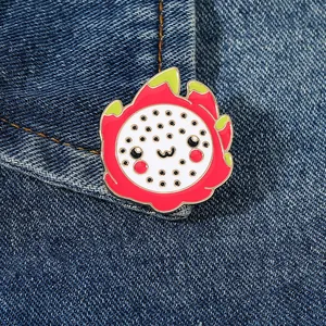 Detailed view of a cute cartoon dragon fruit enamel pin on denim fabric backdrop