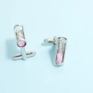 Gros plan de boutons de manchette sablier argenté avec sable rose sur fond bleu clair