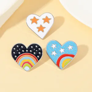 Détails de trois broches cœur en émail arc-en-ciel avec motifs étoilés sur fond beige