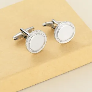 Detail view of round silver metal cufflinks with textured edges in a brown gift box
