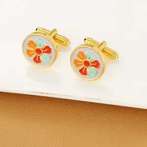 Detailed macro of gold French cufflinks with colorful floral enamel on white display