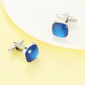 Macro detail of silver square cufflinks featuring blue cat-eye stone inlay and polished finish