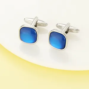 Detailed close-up of square silver cufflinks with blue crystal inlay on a white surface