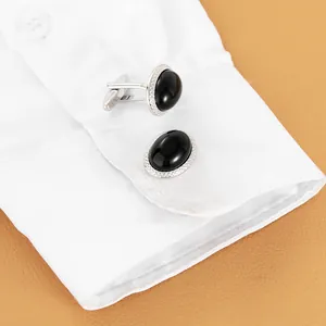Gemelli ovali in argento con pietra nera e cristalli su polsino di camicia bianca