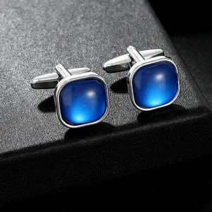Close-up of square blue crystal cufflinks in silver finish on a textured display