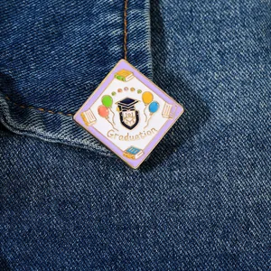 Detail of a diamond-shaped graduation enamel pin with books and balloons on denim jacket