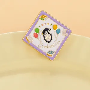 Close-up of square graduation enamel pin with academic cap and colorful balloons
