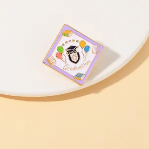 Detail of square enamel graduation pin with mortarboard and balloons on white stand