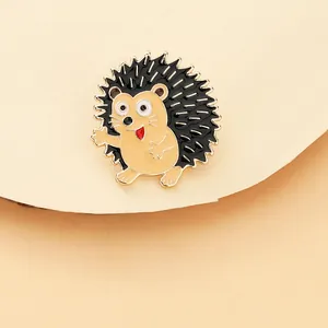 Close-up of a cute cartoon hedgehog enamel pin with gold metal outlines and waving pose