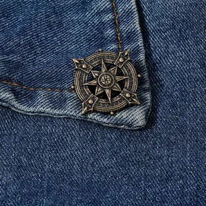 Close-up of retro bronze anchor brooch on dark blue denim fabric with orange stitching