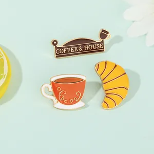 Detailansicht der Emaille-Pins mit Kaffeetasse, Croissant und Caféschild auf blauem Grund