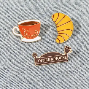Details von Emaille-Anstecknadeln mit Kaffee und Croissant auf Denim-Hintergrund
