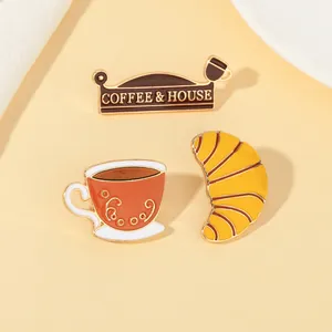 Detailansicht der Emaille-Pins mit Kaffee- und Croissant-Motiv und Goldrand