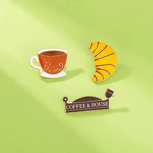 Detailansicht der Emaille-Pins mit Kaffeetasse, Croissant und COFFEE & HOUSE Gravur