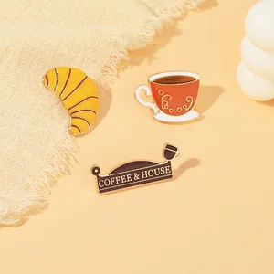 Detailansicht der Emaille-Pins mit Kaffee und Croissant und Goldrand auf warmem Grund