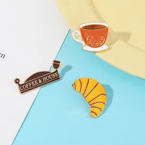 Detailansicht des Emaille-Pin-Sets mit Kaffeetasse, Café-Schild und Croissant auf Blau