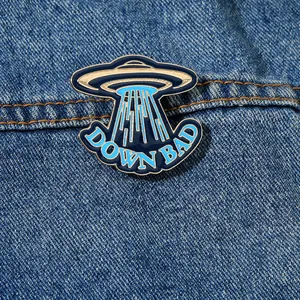 Detailed view of the Down Bad UFO enamel pin on dark denim with gold-toned metal details