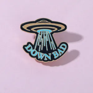Detailed close-up of a UFO enamel pin with DOWN BAD text on light purple background