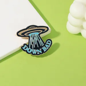 Detail of UFO enamel pin with blue beam and DOWN BAD text on light green background