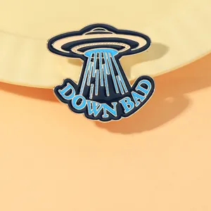 Detail of UFO enamel pin with blue rays and Down Bad lettering in golden metal